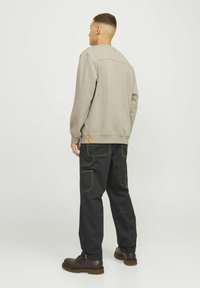 Sweatshirt gris clair avec un ourlet côtelé, associé à un pantalon cargo noir ample avec des coutures blanches et des poches, porté avec des bottes marron.