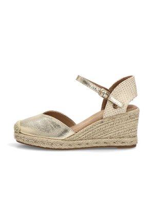 Sandalia cuña de esparto dorada con correa en el tobillo, suela de yute tejida y puntera cerrada sobre fondo blanco.