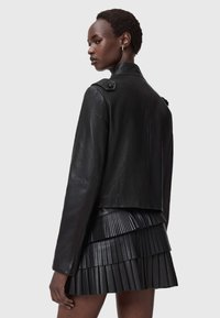 Zwarte leren jas met een gestructureerd ontwerp, voorzien van schouderepauletten en een getailleerde snit. Gepaard met een geplooide zwarte rok.