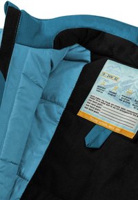 Blaue und schwarze isolierte Jacke mit glatter Textur. Verfügt über ein Etikett mit Pflegehinweisen und eine kontrastierende Stoffschlaufe.