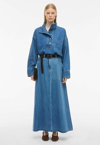 Jeans obleka z visokim ovratnikom, dolgimi rokavi in sprednjim žepom, ki ima pas in dolg kroj v srednje modrem pranju.