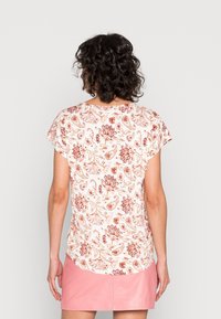 Top ligero de manga corta en color crema con un patrón de paisley floral rojo. Presenta un cuello redondo y un corte holgado, apto para un uso casual.