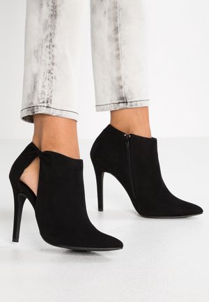 Sorte nubuck ankelstøvler med spids tå, stiletto hæl og lynlås på siden. Har en åben bagdel med en bindedetalje.
