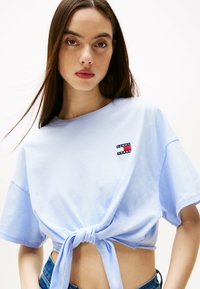 Jasnoniebieska krótka koszulka wykonana z miękkiej bawełny. Posiada zawiązanie z przodu i małe haftowane logo w kolorach czerwonym, białym i niebieskim.