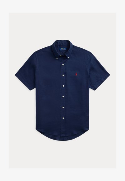 Marineblå kortermet skjorte med knapper laget av lin, med en liten rød logo på brystet og avrundet kant.