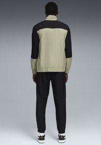 Leicht grüner und schwarzer Sportanzug mit hohem Kragen, elastischen Bündchen und Bund, gefertigt aus glattem, glänzendem Material.