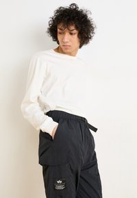 Chemise blanche à manches longues associée à un pantalon cargo noir ample avec une taille élastique et des poches cargo.