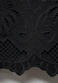 Zwarte stof met complexe borduursels die paisley- en geometrische patronen vertonen, met een gestructureerd oppervlak en gegolfde randen.