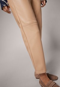 Beige leren broek met een rechte snit, subtiele glans en stikdetails. Gecombineerd met lichtbruine suède instappers.