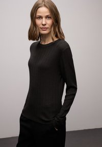 Maglione nero a coste con maniche lunghe e scollo rotondo. Caratterizzato da maniche aderenti e una texture morbida, abbinato a pantaloni scuri. Design semplice.