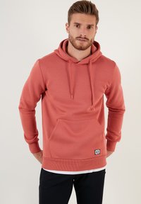 Sudadera de color coral con un bolsillo canguro, capucha con cordón y puños acanalados. La tela es suave, con una textura lisa y un mínimo de marcas.