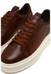 Sneaker in pelle marrone con lacci coordinati, dotati di una suola in gomma bianca testurizzata e accenti di design minimalisti sulla tomaia.