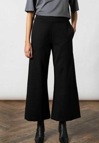 Zwarte wijde broek met een gladde textuur, met een hoge taille en zijzakken, gecombineerd met een grijze top en zwarte enkellaarzen.