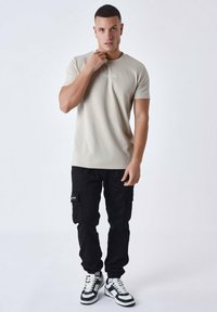 Camiseta texturada de color beige claro con mangas cortas, combinada con pantalones cargo negros con bolsillos laterales, y zapatillas blancas y negras.