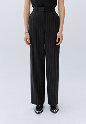 Pantalones de rayas negras y grises con cintura alta, pierna ancha y presillas para cinturón. Tejido suave y líneas limpias; combinados con zapatos negros de punta.