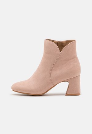 Pale pink suede ankle boot with a pointed toe and v-shaped cutout. Features a medium block heel and a side zipper for easy wear.