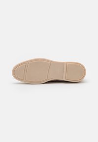 Suola di una scarpa beige con motivi di grip testurizzati e "ANNA FIELD 37" impresso nella parte centrale della suola.