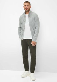 Graue Strickjacke mit Zopfmuster, Knopfverschluss, getragen über einem weißen T-Shirt und olivgrünen Hosen, kombiniert mit weißen Sneakers.