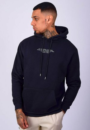 Black hoodie made of cotton blend, featuring a kangaroo pocket, drawstrings, and a small white text design on the front. Smooth texture.