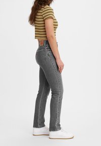 Jeans gris de tiro alto y ajuste slim, con cinco bolsillos, costuras sutiles y una etiqueta de cuero en la cintura trasera. Combinados con una blusa a rayas.