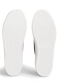 Calvin Klein-skor med två vita gummisulor med texturerade mönster, varje präglad med varumärkets initialer.