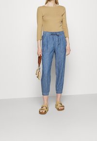 Haut ajusté à manches longues de couleur brun clair, pantalon bleu à cordon de serrage avec une texture rayée, et sandales confortables couleur beige avec une boucle.