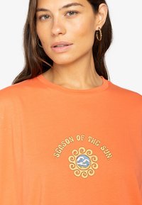 Orange T-shirt made of soft cotton, featuring a round neckline and a graphic design reading "SEASON OF THE SUN" with a sun motif.