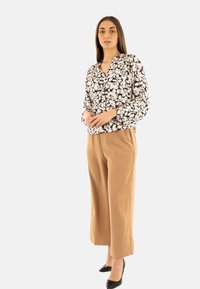 Blusa floral en crema y negro con escote en V y mangas largas, combinada con pantalones beige de pierna ancha de cintura alta y tacones negros de punta.