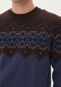 Stickad tröja i mörkbrun och blå med geometriska mönster. Ribbad rund hals och texturerad nedre del. Accenter i crème.