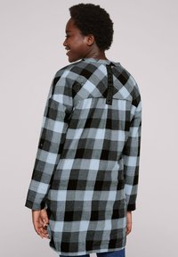 Tunic a maniche lunghe in plaid nei toni di nero, blu e grigio. Presenta un dettaglio sul retro con una striscia texture. Realizzata in morbido tessuto intrecciato.