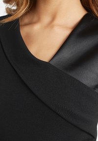 Svart klänning med en satinkrage. Tyget har en strukturerad matt yta som kontrasterar med den släta glansen av kragen.