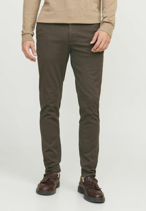 Olivgrüne Hose im Slim-Fit-Stil aus einem glatten, robusten Stoff. Kombiniert mit dunkelbraunen Schuhen im Fransen-Design.