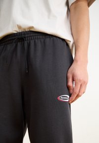 Grå sweatpants med elastisk midja och dragsko, prydda med en framträdande Reebok-logga på vänster sida. Slät bomullstextur.