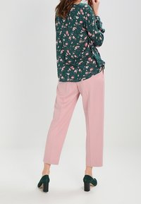 Groene bloemen blouse met lange mouwen, gecombineerd met roze broeken. Accentuert met kleine roze bloemen, van lichte stof en met een relaxte pasvorm. Groene hoge hakken.