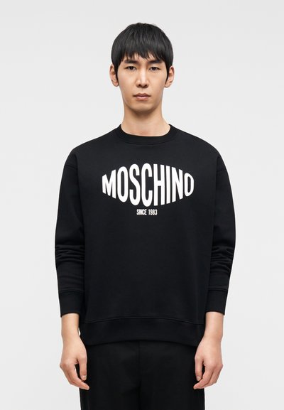 Μαύρο φούτερ από βαμβάκι με στρογγυλή λαιμόκοψη και μακριά μανίκια. Στο μπροστινό μέρος εμφανίζεται με έντονα λευκά γράμματα το λογότυπο "MOSCHINO" και το κείμενο "SINCE 1983".