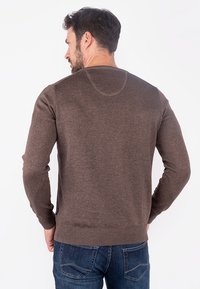 Brown knit sweater with long sleeves and a round neckline, featuring a smooth texture and ribbed hems, worn with blue denim jeans.
