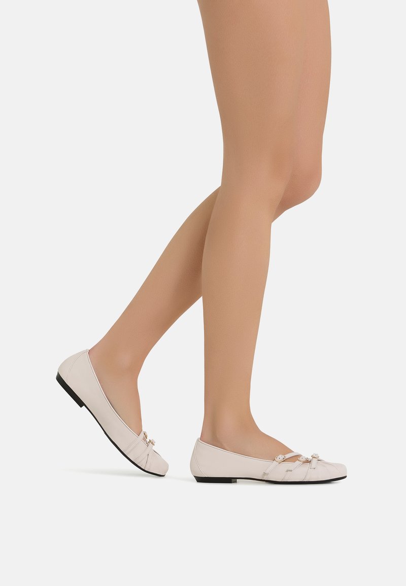 Scarpe piatte rosa chiaro con punta tonda, dotate di un dettaglio a fiocco annodato e di un tacco piccolo e solido nero. Texture liscia e design minimale.