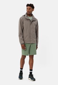 Grijze waterdichte jas met een capuchon, gecombineerd met groene shorts. De outfit bevat zwart-witte gestreepte sokken en blauwe schoenen met oranje accenten.