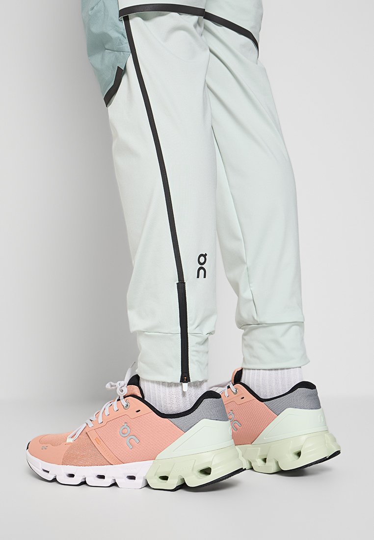 Hellblaue Sporthose mit schwarzen Akzenten, dazu rosa und graue Sneakers mit einer strukturierten Oberseite und einer klobigen weißen und grünen Sohle.