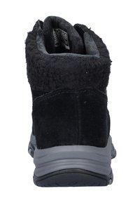 Bota negra de tobillo con parte superior de suave ante, suela de goma gris y forro peludo. Presenta una puntera redondeada y un sutil detalle de costura en el tacón.