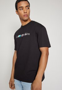 Camiseta de algodón negra con cuello redondo y mangas cortas. Presenta un logo multicolor "Calvin Klein Jeans" estampado en el frente.