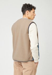Fleece vest met een beige achterkant, blauwe zijpanelen en lange mouwen in crème. Geweven materiaal, geen zichtbare sluitingen, casual ontwerp.