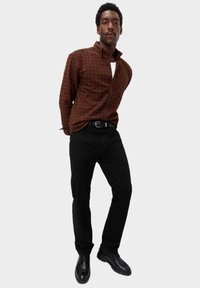 Camisa de cuadros marrón con cuello doblado, combinada con pantalones negros y zapatos de vestir negros. Ajuste simple y entallado.