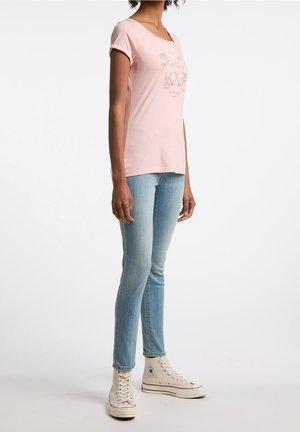 Jasnoróżowa koszulka z krótkim rękawem i okrągłym dekoltem, ozdobiona kolorową grafiką roweru. Połączona z jasnoniebieskimi obcisłymi dżinsami i beżowymi sneakersami.