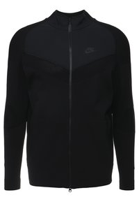 Černá bunda Nike na plný zip s vysokým límcem, texturovanými panely na ramenou a rukávech a subtilním logem Nike na hrudi.