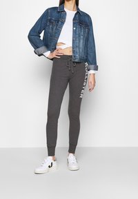 Jeansjacka med ljusblå tvätt, knappstängning fram och uppvikta ärmar; grå joggers med vit "HOLLISTER"-logotyp; vita sneakers.