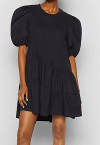 Puffed short sleeve dress in dark navy with a round neckline and tiered ruffle hem. Smooth texture and casual fit.
