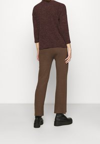 Mörkröd texturerad topp med trekvartslånga ärmar, i kombination med ribbade bruna byxor. Svarta kraftiga stövlar fulländar outfiten.