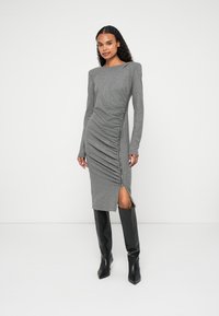 Siva haljina dugih rukava s prilagođenim krojem, bočnim naborima i detaljem zatvarača na bedru. U paru s crnim čizmama do koljena.