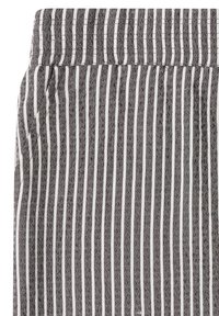 Gros plan sur un tissu à rayures verticales noires et blanches avec un motif texturé subtil, montrant une ceinture et un détail de couture.